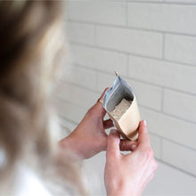Load image into Gallery viewer, Person holding a small container of powder against a tiled wall.
